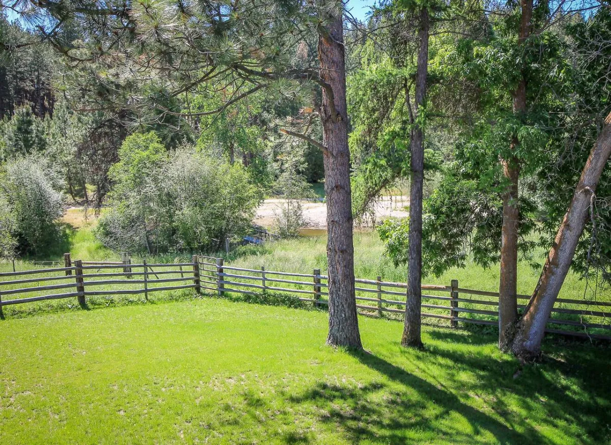 A peaceful exterior scene of lush green grass bordered by a wooden fence, tall trees, and a distant river. The open space invites picnicking, wildlife watching, and outdoor relaxation, highlighting the tranquility and natural beauty of the property.