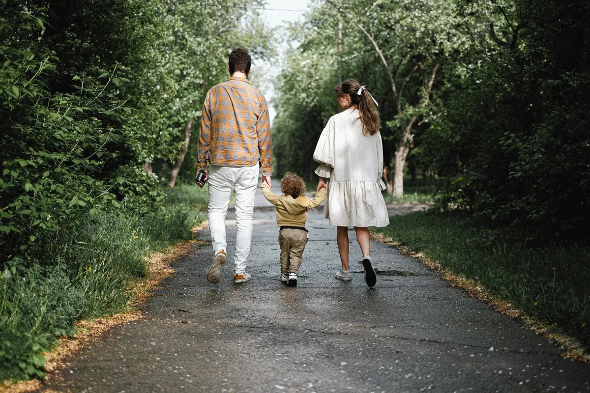 A family walks together along a scenic pathway surrounded by lush greenery. The image conveys a sense of connection and shared adventure, with parents and children exploring the outdoors together. The background features trees and soft natural light, enhancing the mood of joyful togetherness.
