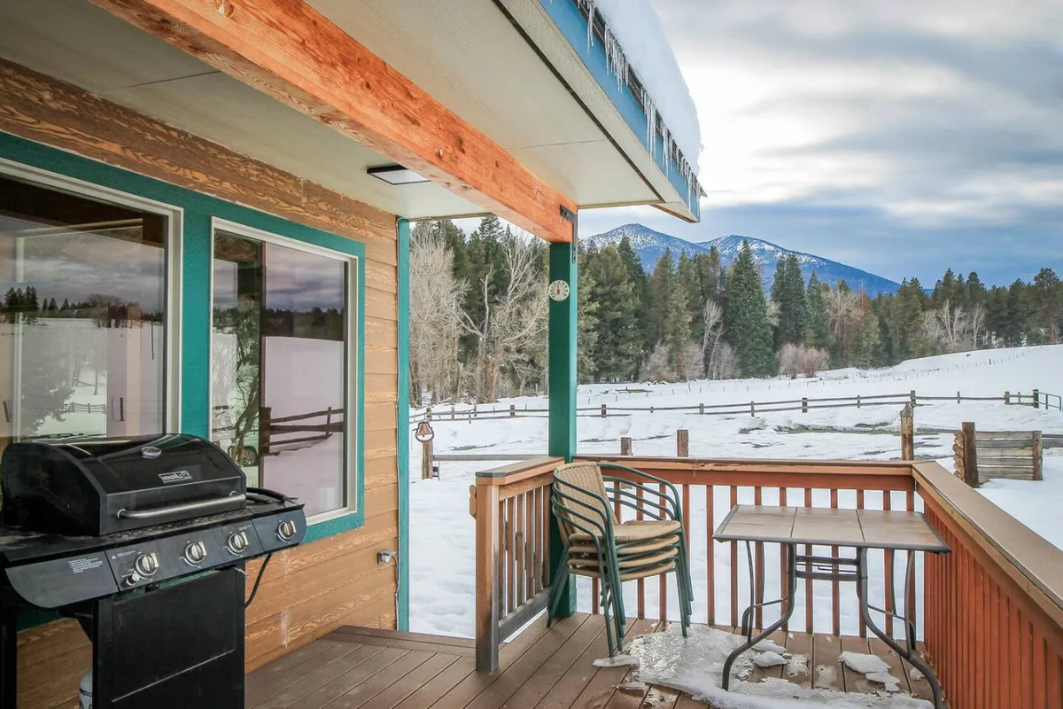 A cozy outdoor setting featuring a grill and seating area on a deck, overlooking a snow-covered landscape with mountains in the distance. The peaceful winter scene invites guests to relax and unwind after a day of adventure.