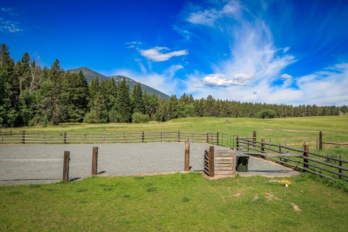 A sweeping view of green pastures, a fenced area, and majestic mountains in the background. The image captures the essence of open ranch living, with hints of outdoor activities and seasonal changes in the landscape.
