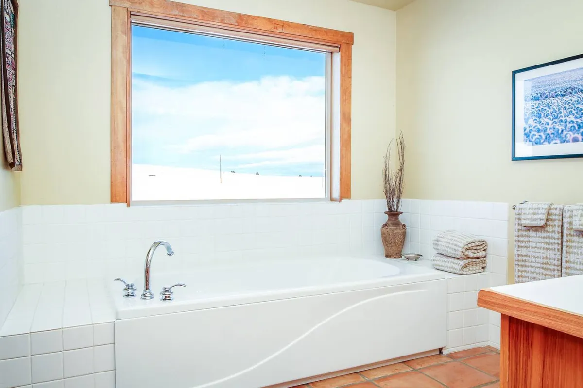 A tranquil bathroom featuring a luxurious bathtub positioned by a window that provides scenic views. Decorative touches like a vase and plush towels evoke a sense of spa-like relaxation and indulgence.