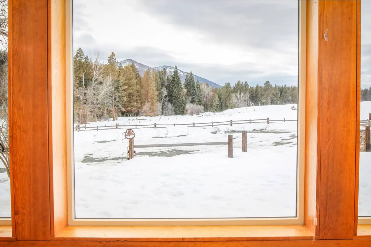 A wide, tranquil view of snow-covered ground with distant mountains, a tree line, and a rustic fence. The scene is peaceful and expansive, hinting at the outdoor spaces and panoramic views available to guests for evening strolls or moments of reflection after a productive day.