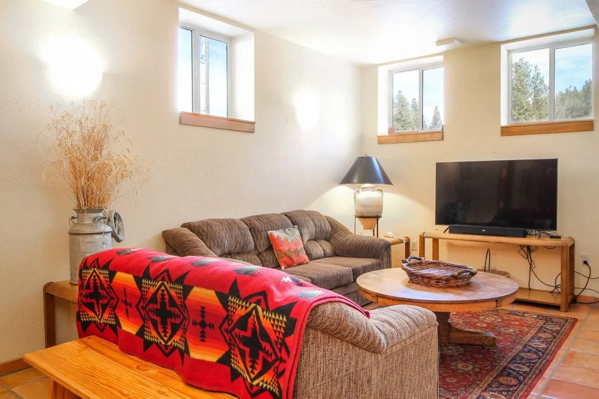 A comfortable living area with a plush sofa draped in a colorful blanket, a wooden coffee table, and a television. The space is bathed in soft light, creating a relaxing atmosphere for watching movies, reading, or enjoying a hot drink while snow falls outside.