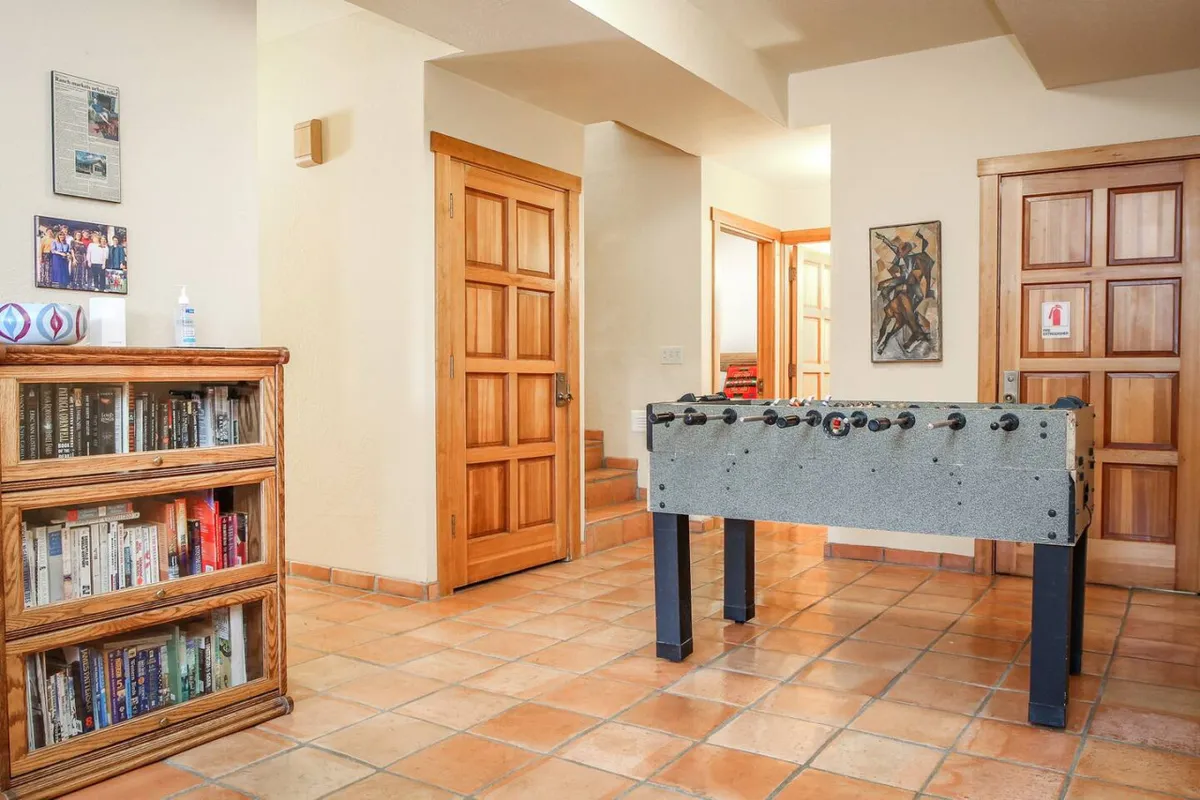 A cozy recreation area with a foosball table, bookshelf filled with books, wooden doors, and colorful artwork on the wall. The scene exudes a casual, welcoming environment ideal for friendly competition, reading, or conversation.